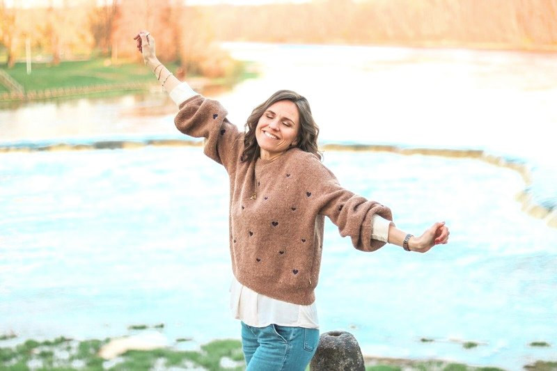 Katharina Pohl am Fluss, Arme ausgebreitet, lachend