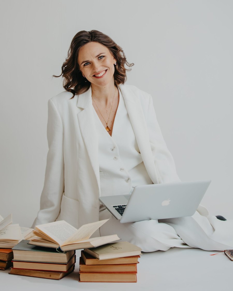 Katharina Pohl im weißen Anzug mit Laptop und Büchern, lächelnd in die Kamera